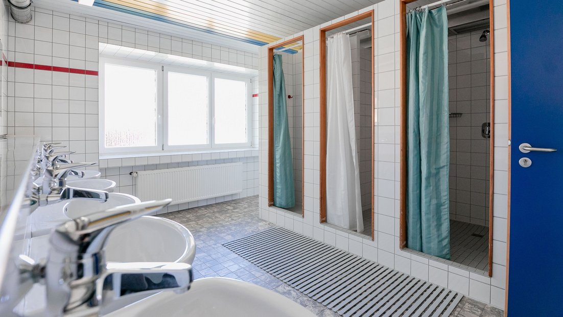 Ванная комната, выложенная белой плиткой в беседке с несколькими раковинами и душевыми кабинами